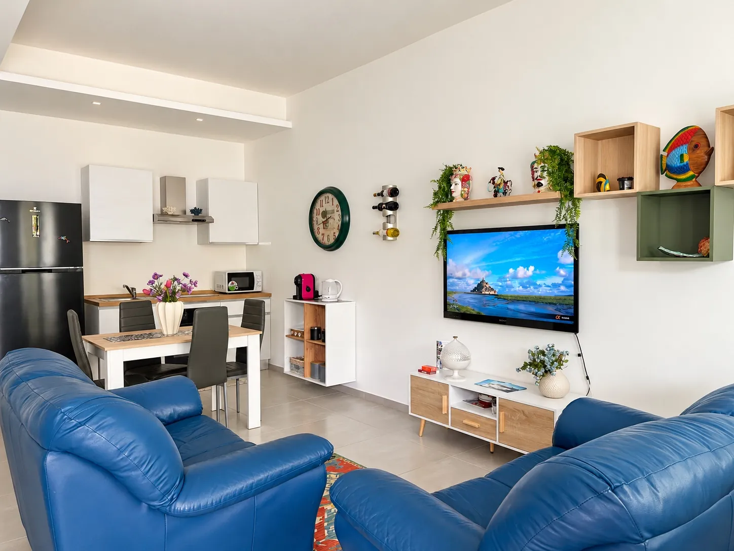 Il soggiorno dell'appartamento con i due divani in pelle blu, la TV e la cucina sullo sfondo