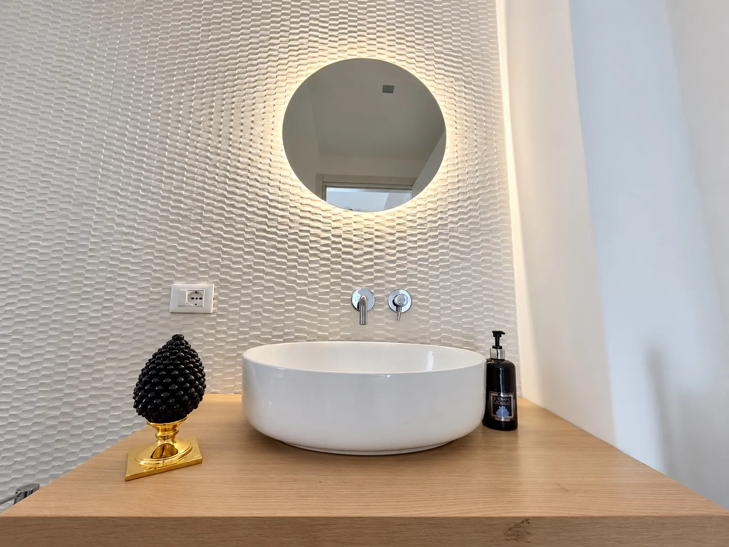 Il lavabo a bacinella del monolocale sotto lo specchio tondo retroilluminato