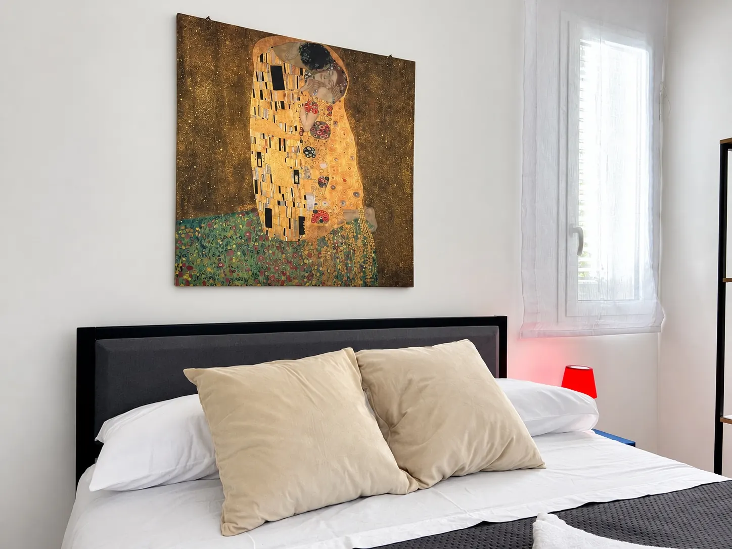 Il letto matrimoniale del monolocale, con i cuscini beige e il quadro sopra la testiera