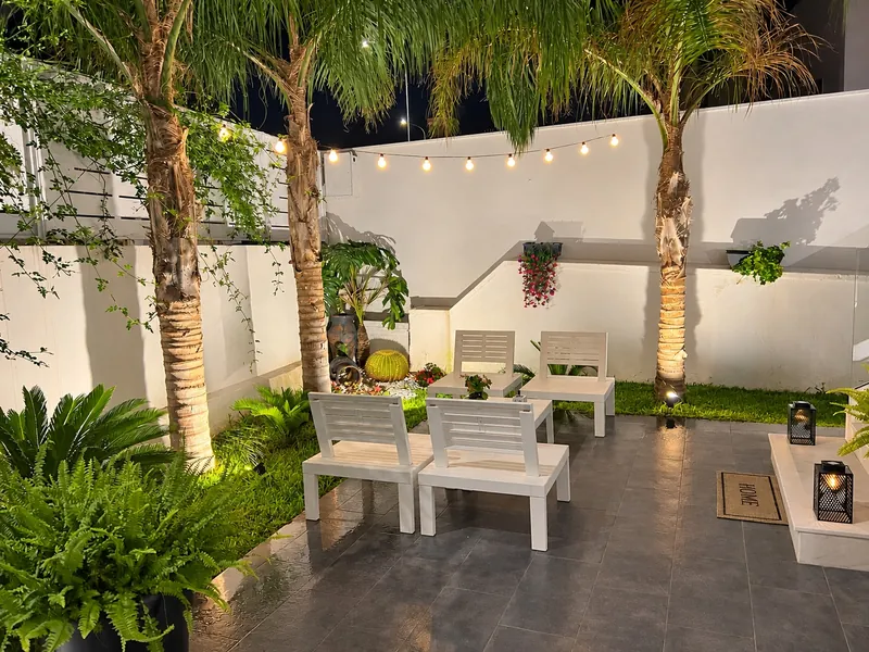 Un angolo del cortile di sera, con la panchina bianca sotto un filo di luci e le palme illuminate