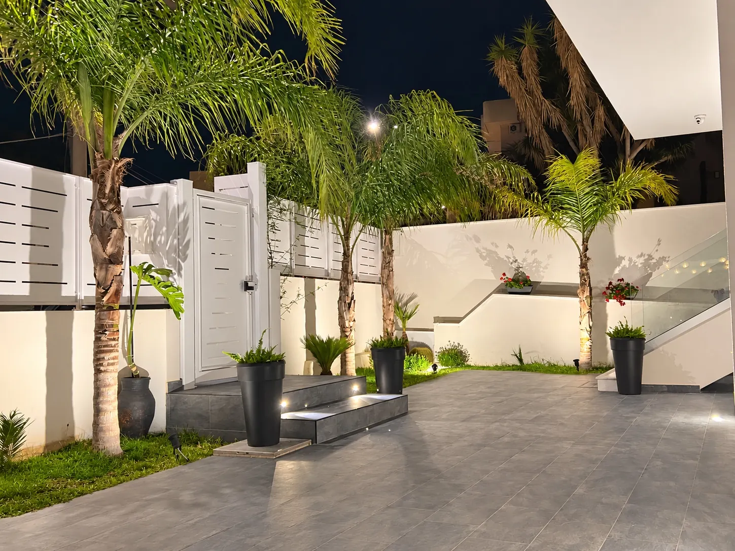 Il cortile della villetta di sera, con le palme illuminate dai faretti