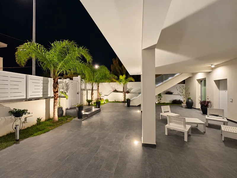 Il cortile coperto della villetta di sera, con le palme illuminate e le sedute bianche