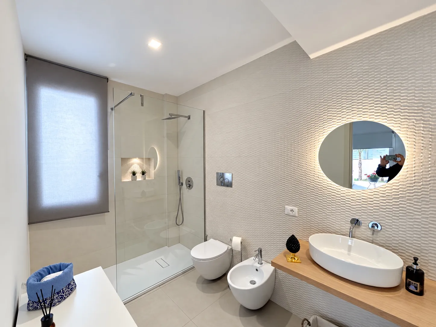 Il bagno del monolocale con la doccia in vetro, il bidet, il lavabo e lo specchio tondo illuminato