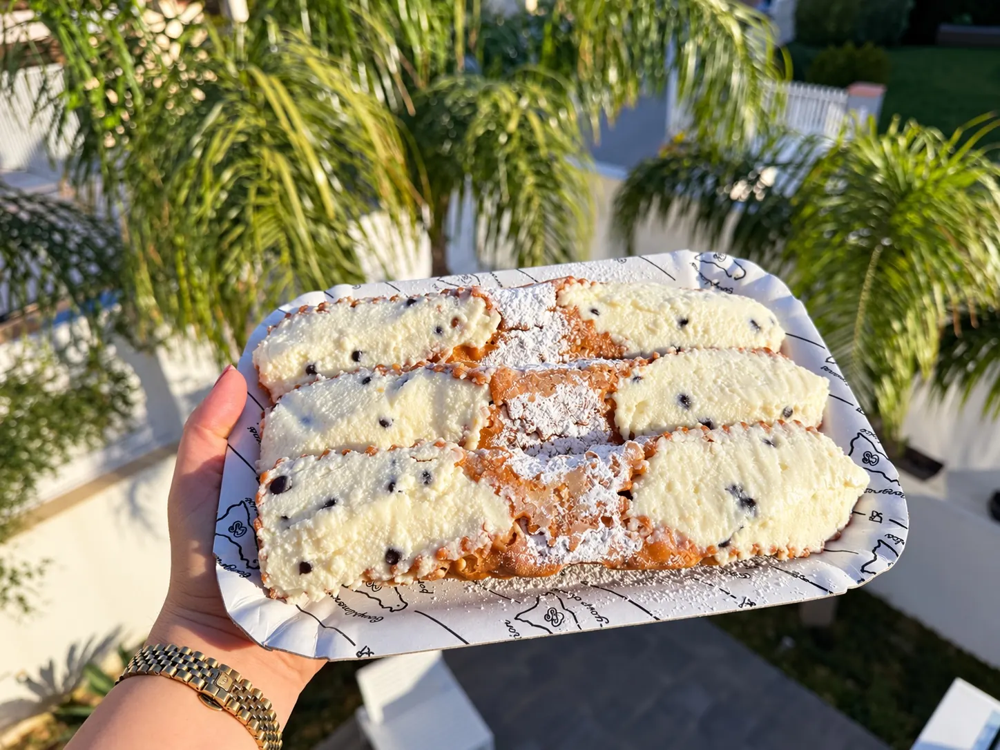 Un vassoio di cannoli siciliani con la ricotta e le gocce di cioccolato, con le palme sullo sfondo
