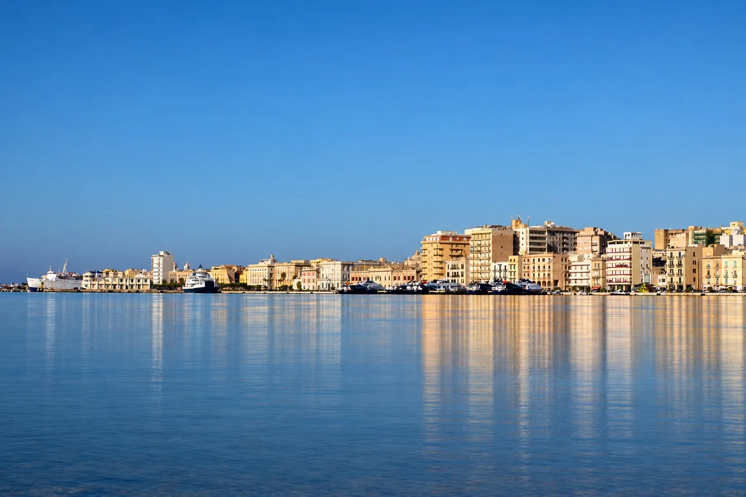 Il lungomare di Trapani visto dal mare, con i palazzi riflessi nell'acqua calma